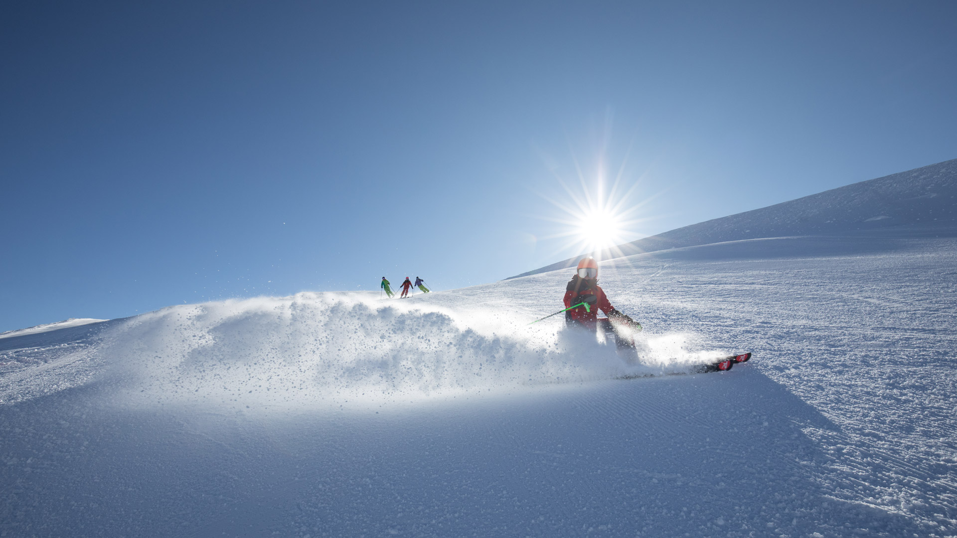 Skifahrer ziehen elegante Schwünge durch den frischen Pulverschnee bei strahlendem Sonnenschein in den Alpen.